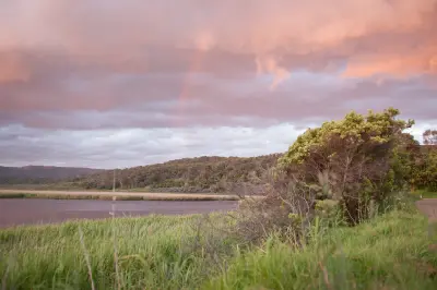 Faint rainbow over the Aire River, reed beds and forested hills in Great Otway National Park, Victoria.