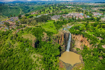 Aerial view of Howick Falls plunging into a deep forested gorge surrounded by green parkland and the town of Howick in KwaZulu-Natal, South Africa.