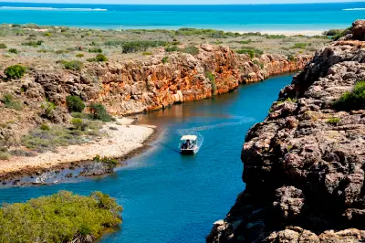 Tour boat travels through the blue waters of Yardie Creek Gorge between rugged red-rock cliffs.