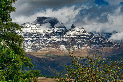 Champagne Castle covered in snow beneath dramatic storm clouds, with layered cliffs and winter conditions in the Central Drakensberg, KwaZulu-Natal, South Africa.