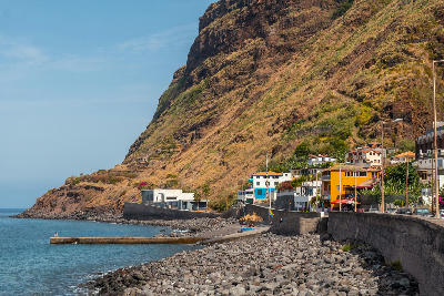 Stone beach at Paul do Mar, with dark pebbles along the shoreline beneath steep volcanic slopes and coastal houses.