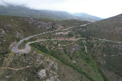 Drone view of the winding hairpin roads of Franschhoek Pass crossing mountainous fynbos landscapes in the Western Cape of South Africa.
