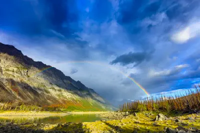 Rainbow arching over Medicine Lake with mountain slopes, dramatic sky, and rocky shoreline