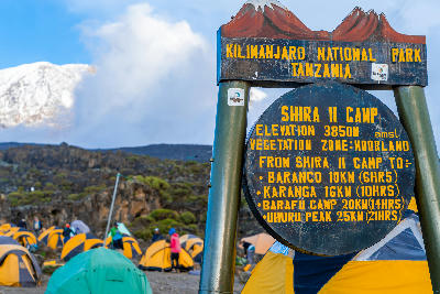 Official Shira II Camp sign beside expedition tents on Mount Kilimanjaro, Tanzania, marking an altitude of 3,850 metres above sea level with Kibo rising in the background.