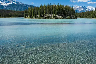 Clear shallow Athabasca River with forested island and mountain backdrop in Jasper National Park