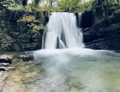 Front view of Janet's Foss waterfall flowing into a clear pool, surrounded by moss-covered rocks and woodland near Malham, North Yorkshire.