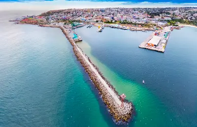 Aerial view of Mossel Bay Harbour and breakwater with the town skyline in the background, Western Cape, South Africa.