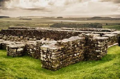 Weathered stone ruins at Housesteads Roman Fort in Northumberland beneath dramatic cloudy skies, with open countryside beyond.