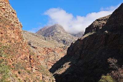 Red sandstone canyon walls and rugged mountain peaks in Meiringspoort within the Swartberg Mountains of the Western Cape, South Africa.