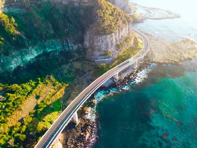 Aerial sunrise view of Sea Cliff Bridge curving beneath steep coastal cliffs above the turquoise waters of the Tasman Se
