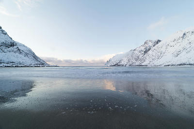 Calm shoreline reflections on Ersfjord with snow-covered mountains on Senja