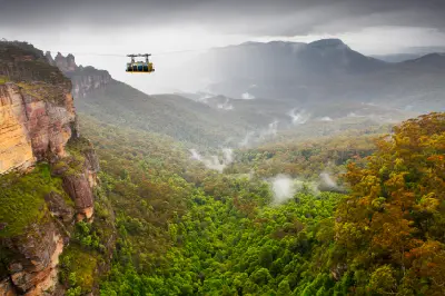 Cable car crosses a vast forested valley between sandstone cliffs as mist drifts through the Blue Mountains.
