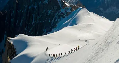 Climbers walking down a narrow snow ridge from Aiguille du Midi onto the Vallée Blanche glacier in the French Alps.