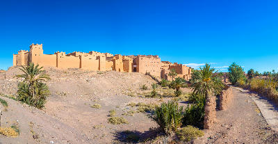 Taourirt Kasbah fortress in Ouarzazate, Morocco surrounded by arid desert terrain, palm trees, and traditional earthen defensive walls
