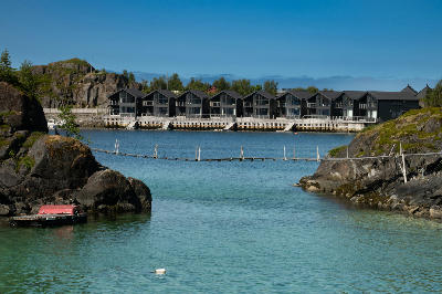 Rorbu cabins at Hamn i Senja seen across calm turquoise water between rocky coastal outcrops