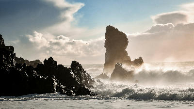 Waves crashing against volcanic rock formations at Djúpalónssandur beach on the Snæfellsnes Peninsula in Iceland, with sea spray rising around jagged cliffs.