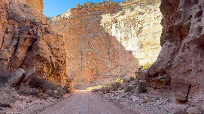 Dirt road passing between steep sandstone canyon walls in Capitol Gorge showing layered rock formations in Capitol Reef National Park Utah