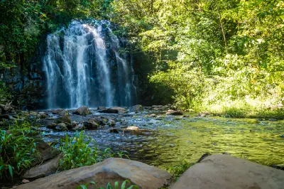 Ellinjaa Falls flowing into a rocky rainforest creek, with sunlight illuminating the surrounding vegetation in the Atherton Tablelands, Queensland.