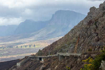 Mountain road and viaduct along Sir Lowry’s Pass beneath the Hottentots Holland Mountains under storm clouds in the Western Cape, South Africa.