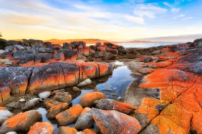 Orange lichen-covered granite rocks and tidal pools at The Gardens, Bay of Fires, Tasmania.