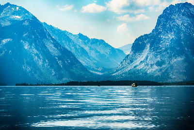 Single boat on Jackson Lake with layered Teton Range mountains in Grand Teton National Park, Wyoming, USA.