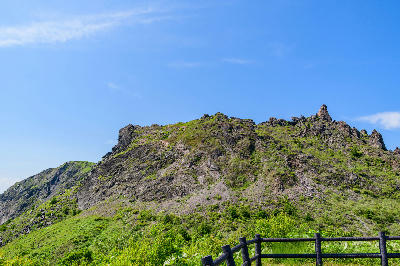 Rocky ridge of Mount Usu with green vegetation under a clear blue sky in Hokkaido, Japan.