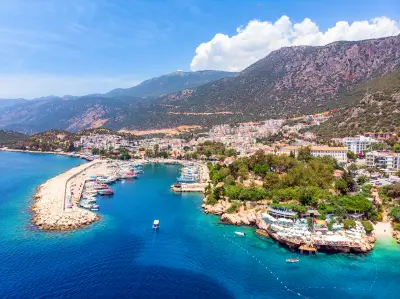 Aerial view of Kaş, with boats in the sheltered harbor, turquoise Mediterranean water, and the town rising toward rugged mountains.