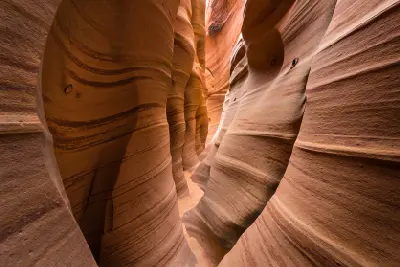 Narrow passage with curved red and pink banded sandstone walls inside Zebra Slot Canyon, Utah.