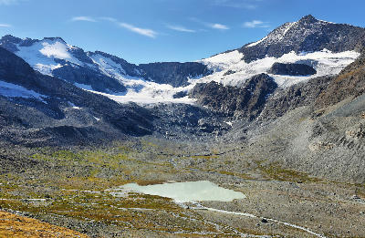 Alpine glacier above a rocky cirque with a small glacial lake in the foreground in Vanoise National Park