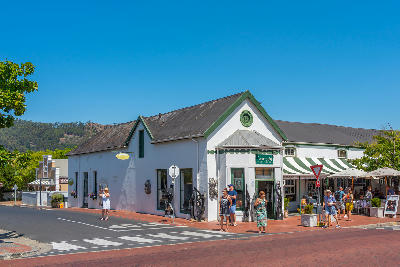Street scene in Franschhoek Village with visitors, cafés, boutique shops, and Cape Dutch-style buildings in the Western Cape wine region.