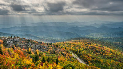 Sun rays shining across colourful autumn ridges and the Blue Ridge Parkway viewed from Rough Ridge on Grandfather Mountain.