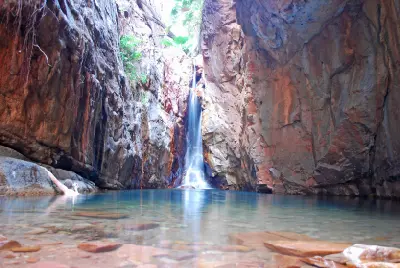 wimmer in a clear rock pool beneath a waterfall enclosed by towering red walls in El Questro Gorge.