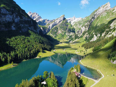 Aerial view of Seealpsee surrounded by green alpine slopes, forest, and valley paths in the Alpstein mountains, Switzerland.