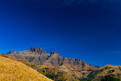 Champagne Castle towering above the grass-covered hills of Cathkin Valley in the Central Drakensberg, KwaZulu-Natal, on a clear winter morning.