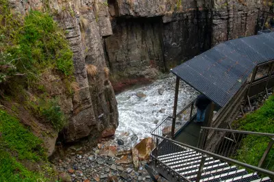 Metal stairs descending between steep rock walls toward Remarkable Cave at Maingon Bay, Tasmania.