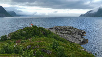 Elevated view from Husøy showing rocky shoreline, small beacon, and open fjord water framed by distant mountains