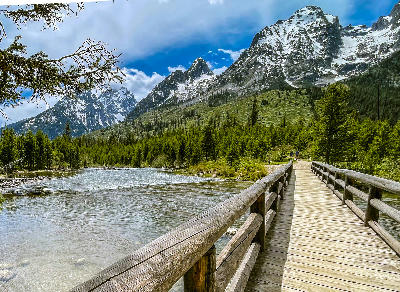 Wooden footbridge over water at Jenny Lake with forest and the Teton Range in the background, Grand Teton National Park, Wyoming, USA.