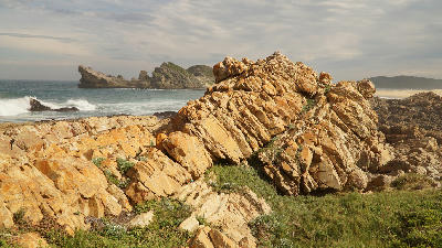 Rocky coastal landscape with ocean waves and Robberg Peninsula in the distance at Robberg Nature Reserve, South Africa.
