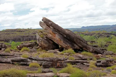 Large tilted sandstone rock formation surrounded by weathered rocky outcrops and sparse vegetation at Ubirr in Kakadu National Park, Australia.