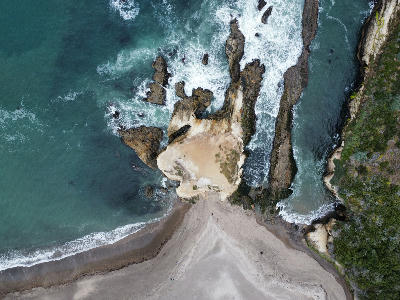 Aerial view of layered sandstone formations and ocean waves at Spooner’s Cove in Montaña de Oro State Park, California.