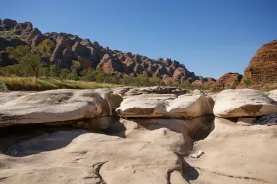 Smooth eroded rock in a dry creek bed beneath the distinctive striped sandstone domes of the Bungle Bungle Range.
