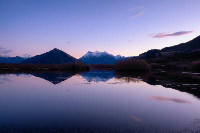 Snow-capped mountains reflected in the calm waters of Glenorchy Lagoon at dawn near Glenorchy, South Island, New Zealand.