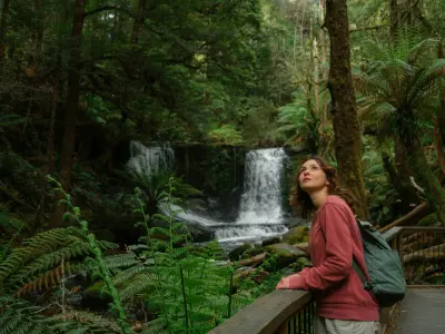 Woman viewing Horseshoe Falls cascading through dense green rainforest in Mount Field National Park, Tasmania.