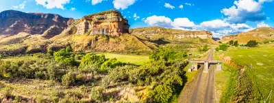 Panoramic view of Golden Gate Highlands National Park with sandstone cliffs, grassland valleys, a winding road and the Maloti Mountains rising in the background.
