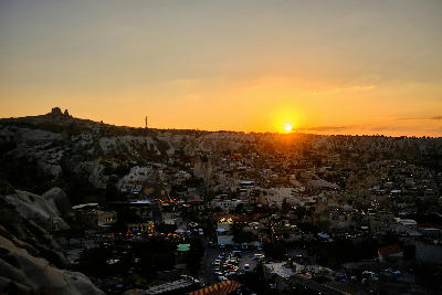 Sunset over Göreme Town in Cappadocia with cave hotels, fairy chimneys and Uçhisar Castle silhouetted against a golden sky, Turkey.