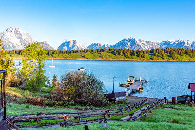 Jackson Lake with dock, boats, and wooden fence in foreground and Teton Range at sunrise in Grand Teton National Park, Wyoming, USA.