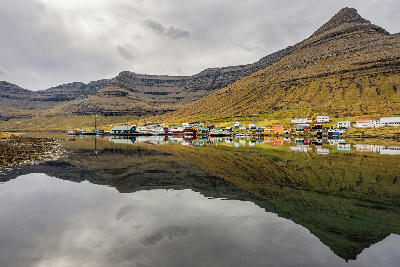 View of Norðdepil reflected in the fjord beneath layered mountains on Borðoy in the Northern Islands of the Faroe Islands.