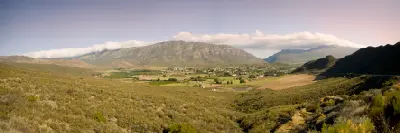 Wide landscape panorama of Barrydale with farmland, valley vegetation, and the Langeberg mountain range under low cloud in the Western Cape, South Africa.