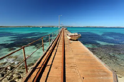 View along Vivonne Bay's wooden jetty with a small fishing boat, metal railings and turquoise water on Kangaroo Island, South Australia.