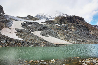 Glacial lagoon beneath rocky slopes with remnant ice and snow patches in Vanoise National Park